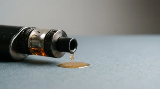 Clearomiseur incliné sur une surface épurée avec une goutte d'e-liquide qui s'échappe, symbolisant le gaspillage annuel de flacons